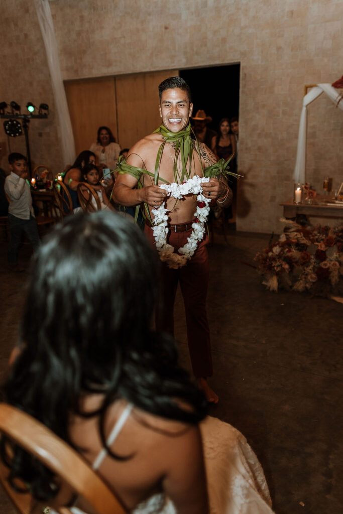 shirtless groom giving a lei to the bride