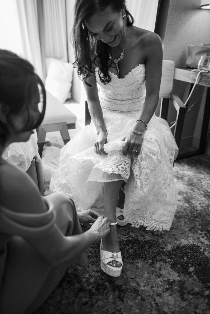 bridesmaid helping the bride put on her heels in black and white