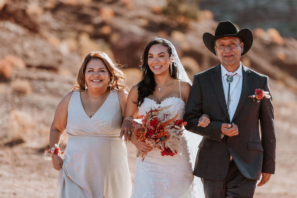 the bride and her parents walking down the isle at the red earth venue in moab utah