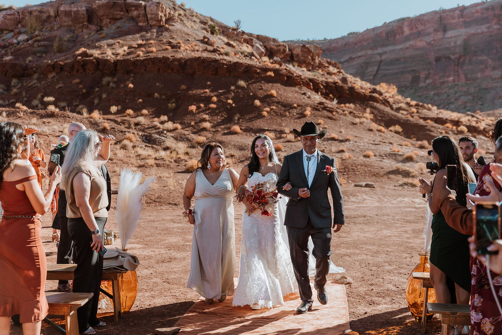 the bride and her parents walking down the isle at the red earth venue in moab utah