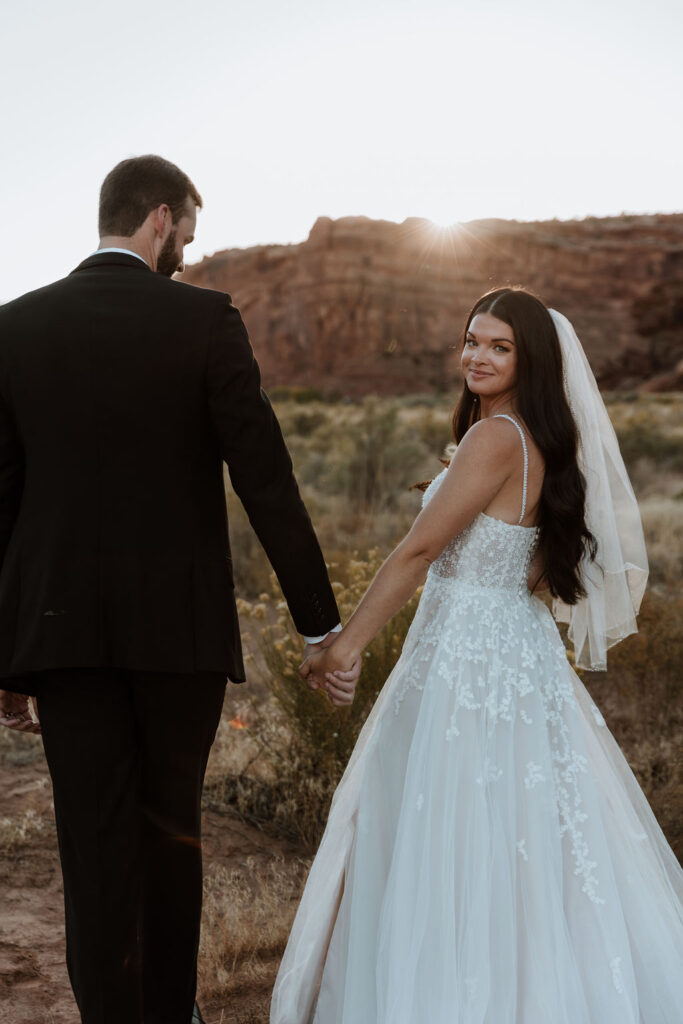 couple holds hands in field at sunset elopement 