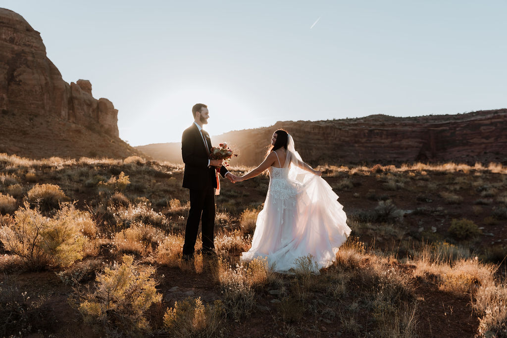 couple holds hands in field at Moab elopement