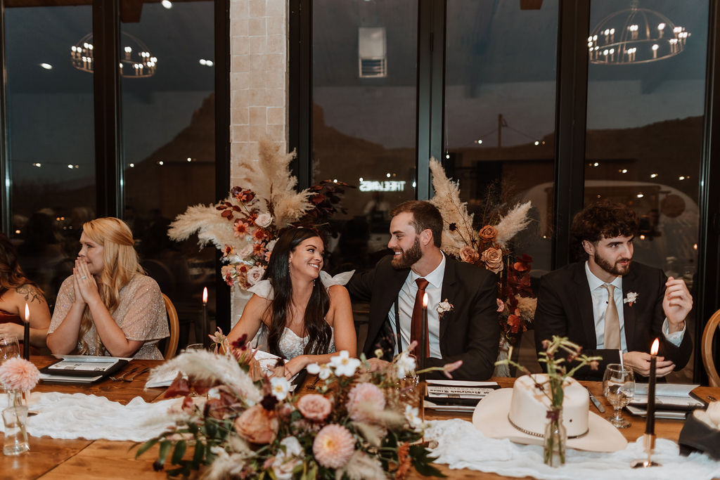 couple sits with wedding party at rustic wedding reception