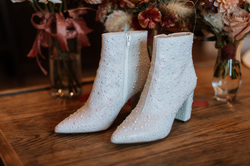 pearl-studded white leather ankle boots beside wedding florals