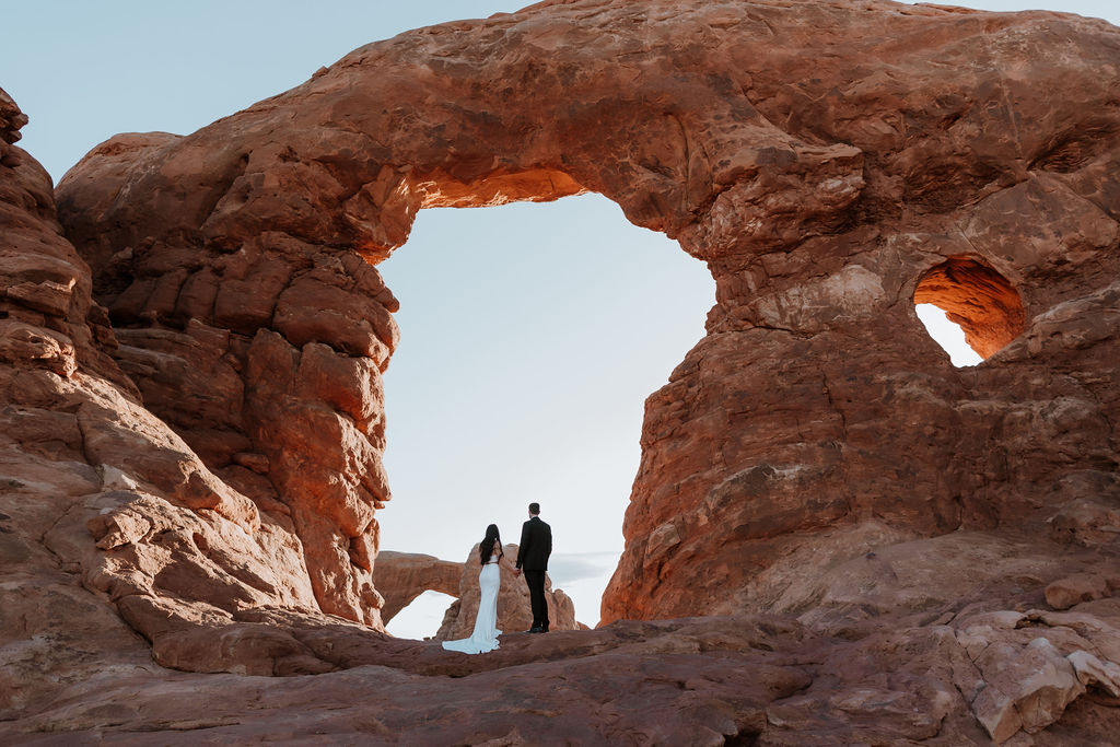 couple stands under arch at Arches National Park sunrise elopement
