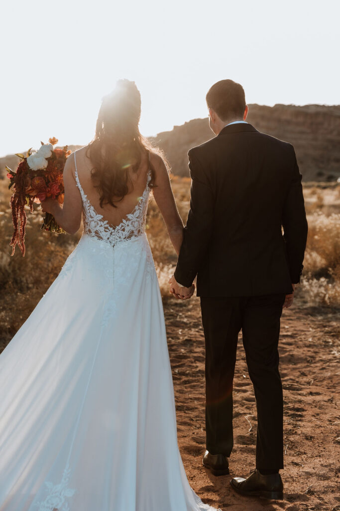 couple walks holding hands in field at Moab sunset elopement