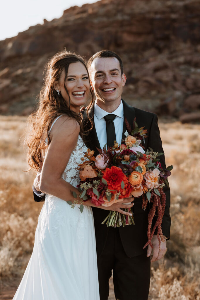 couple laughs holding colorful wedding bouquet at Moab elopement
