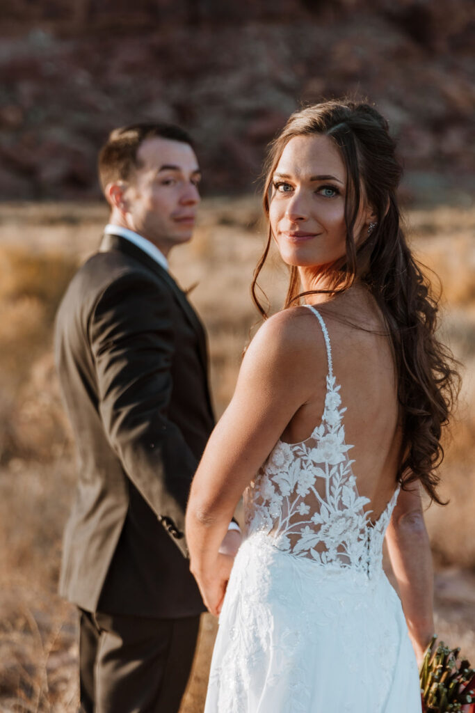 couple walks holding hands in field at Moab sunset elopement