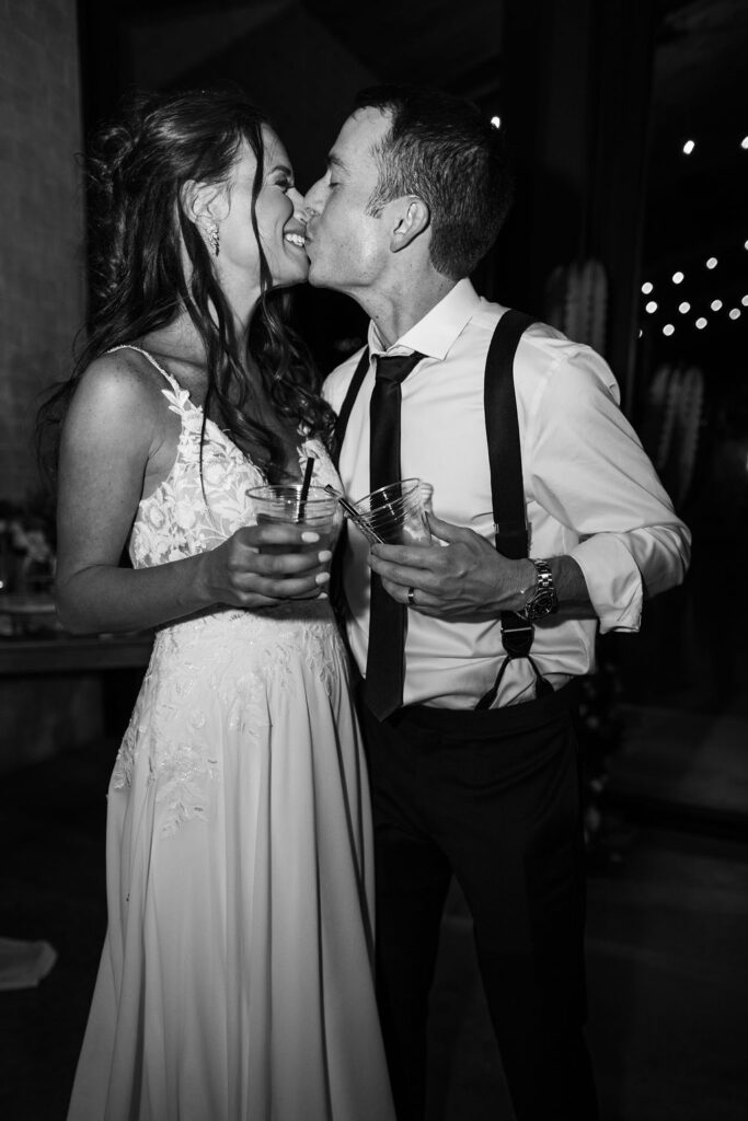 couple kisses holding drinks at wedding reception