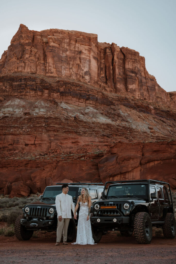 couple poses with Jeeps at Moab sunset desert elopement