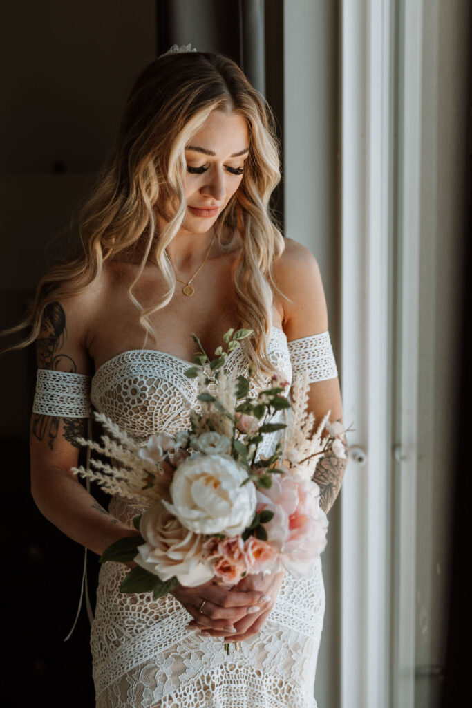 bride poses in window light holding boho wedding bouquet 