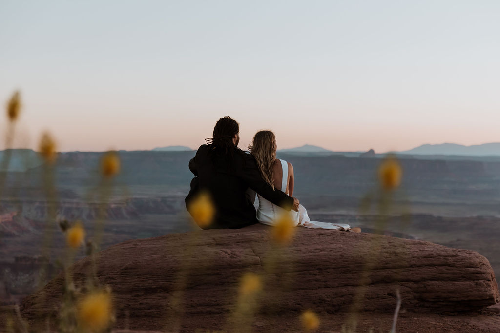 couple sits on ledge watching Moab desert sunset