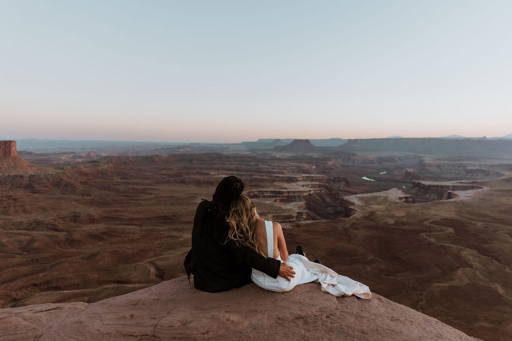 bride and groom sit on edge at Moab couples adventure