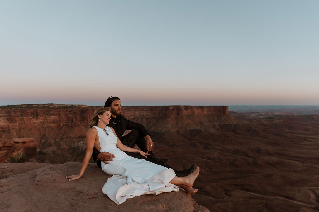 couple sits on overlook at sunset Moab elopement