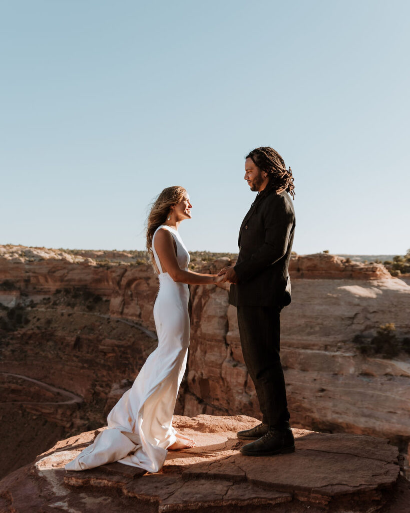 bride and groom stand on edge at Moab couples adventure