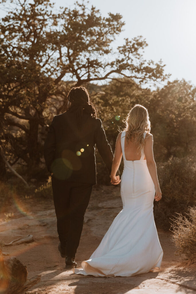 bride and groom walk holding hands at couples adventure in Moab