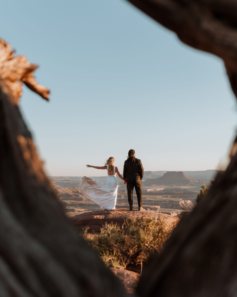 bride and groom stand on edge at Moab couples adventure