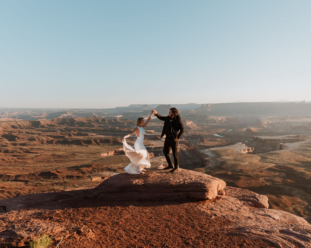 bride and groom twirl on edge at Moab couples adventure