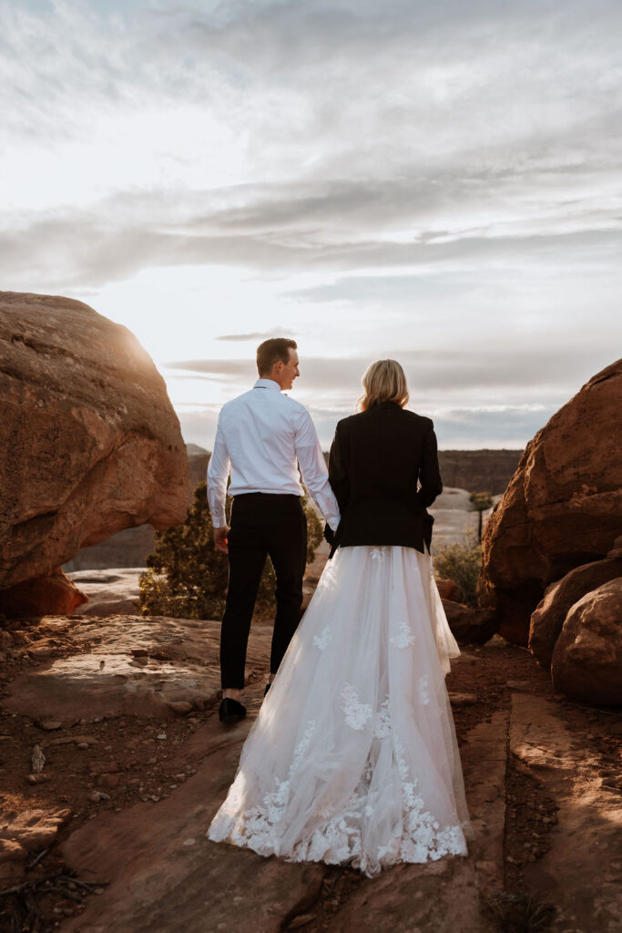 couple walks holding hands at Moab sunset