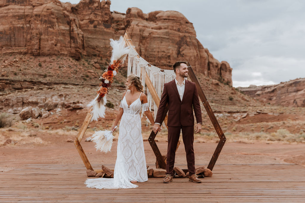 couple holds hands in front of boho wedding decor