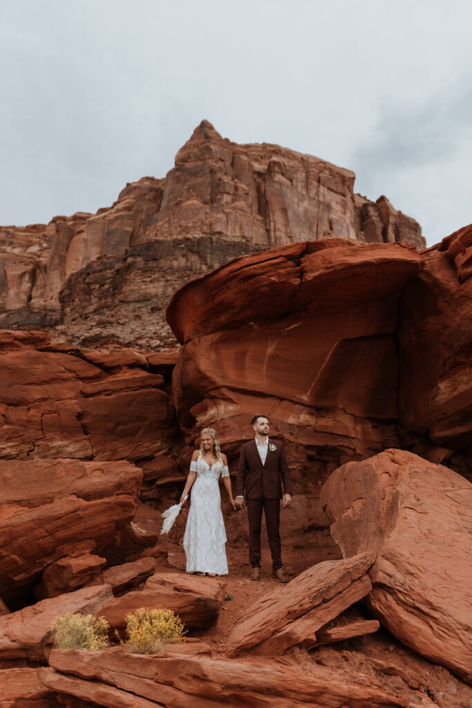 couple holds hands in front of Moab red rocks