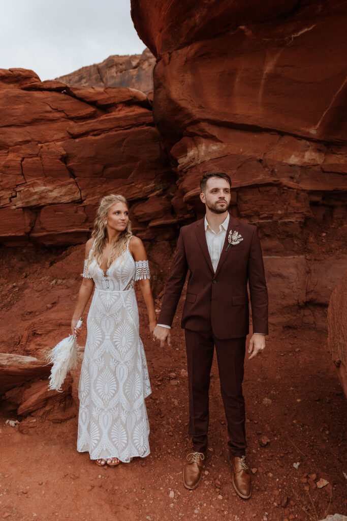 couple holds hands in front of Moab red rocks