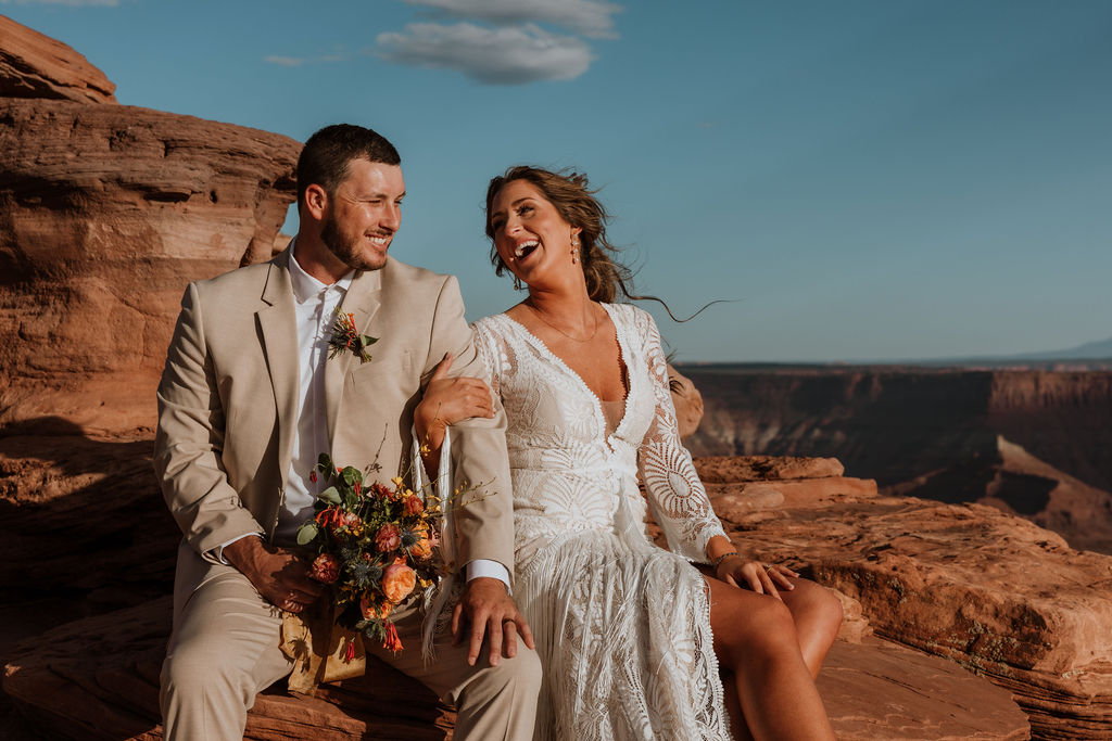 couple laughs together at sunset Moab overlook elopement