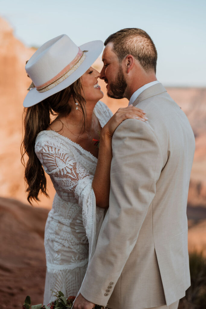 bride kisses groom while wearing hat at wedding first look