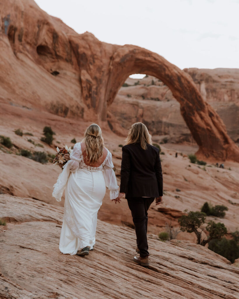 couple walks approaching arch at Bureau Land Management land