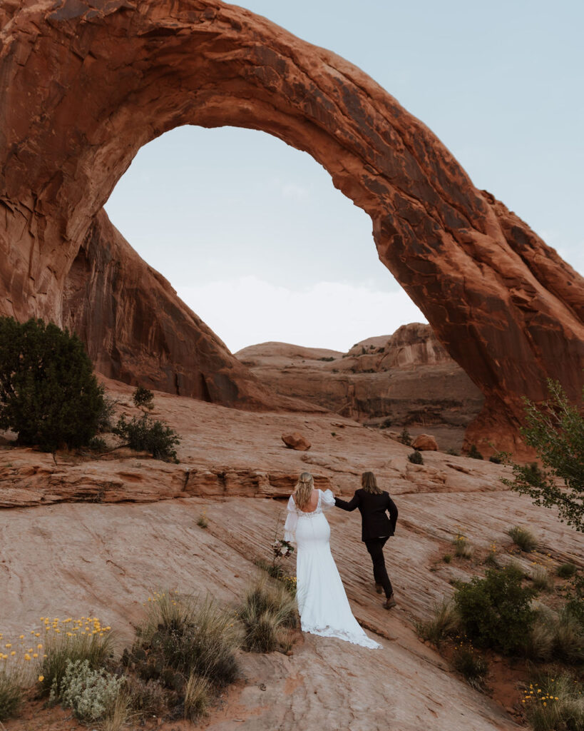 couple walks approaching arch at Arches National Park elopement