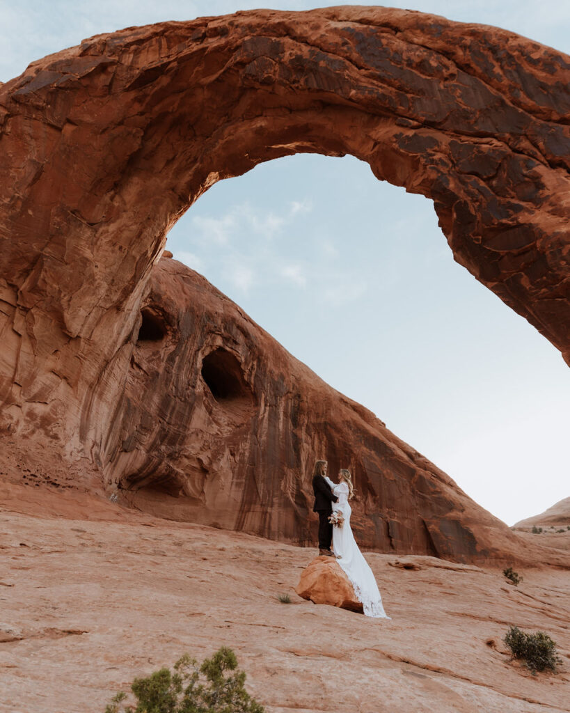 couple poses under arch at Arches National Park elopement