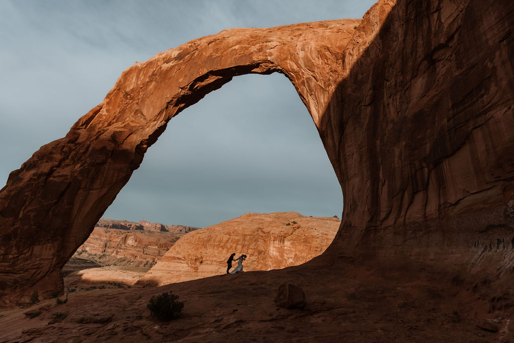 couple walks under arch at Arches National Park elopement