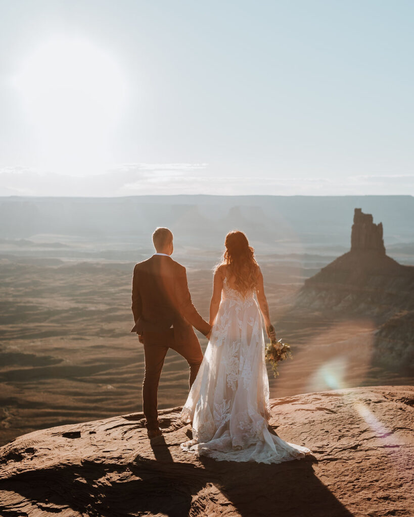 couple holds hands at edge of rock at Moab elopement