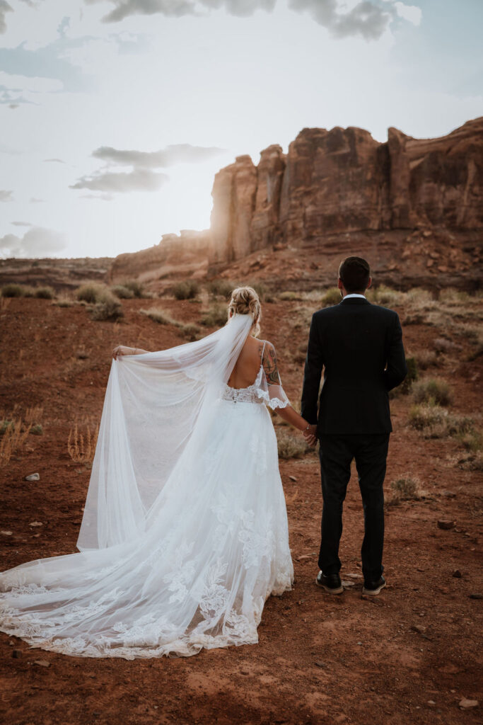 couple holds hands in Moab desert at sunset