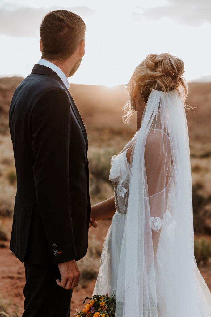 couple holds hands in Moab desert at sunset