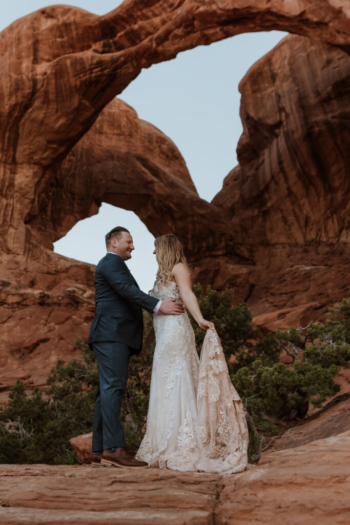 couple stands under arch at Arches National Park elopement