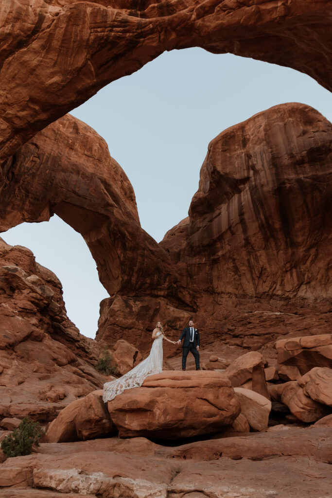 couple stands under arch at Arches National Park elopement