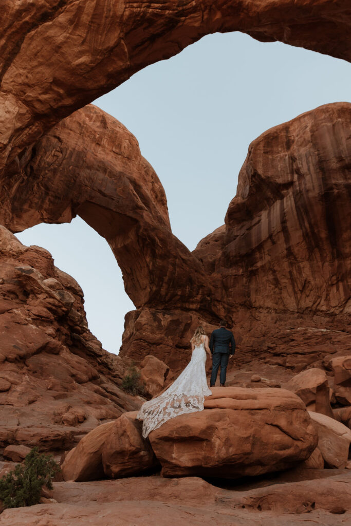 couple stands under arch at Arches National Park elopement