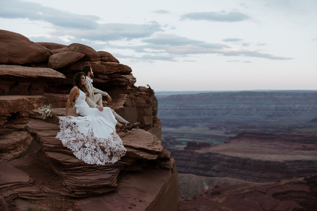 couple sits on edge of rock at Moab elopement