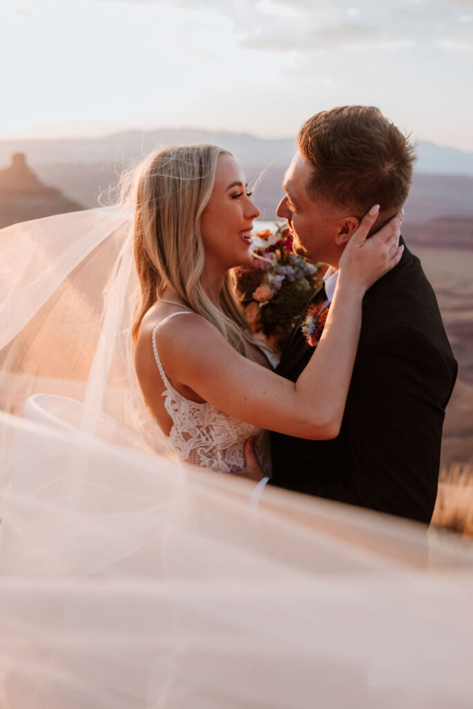 couple kisses under veil at Moab sunset elopement