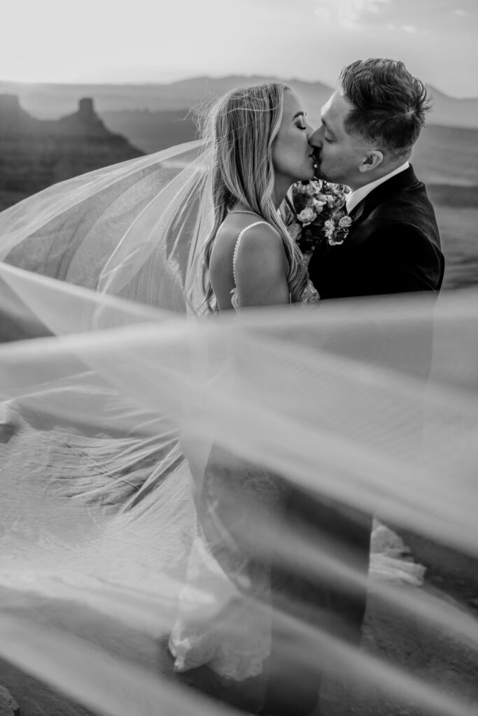 couple kisses under veil at Moab sunset elopement