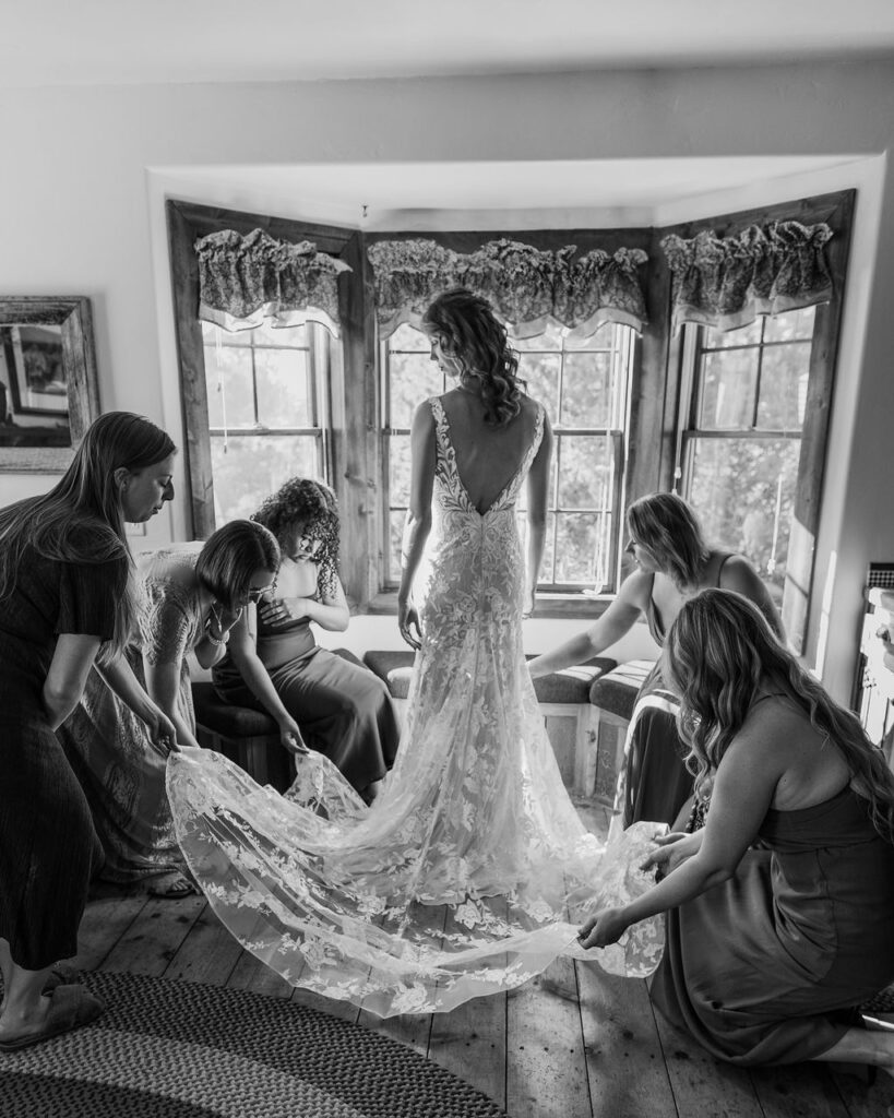 bride poses with bridesmaids holding dress