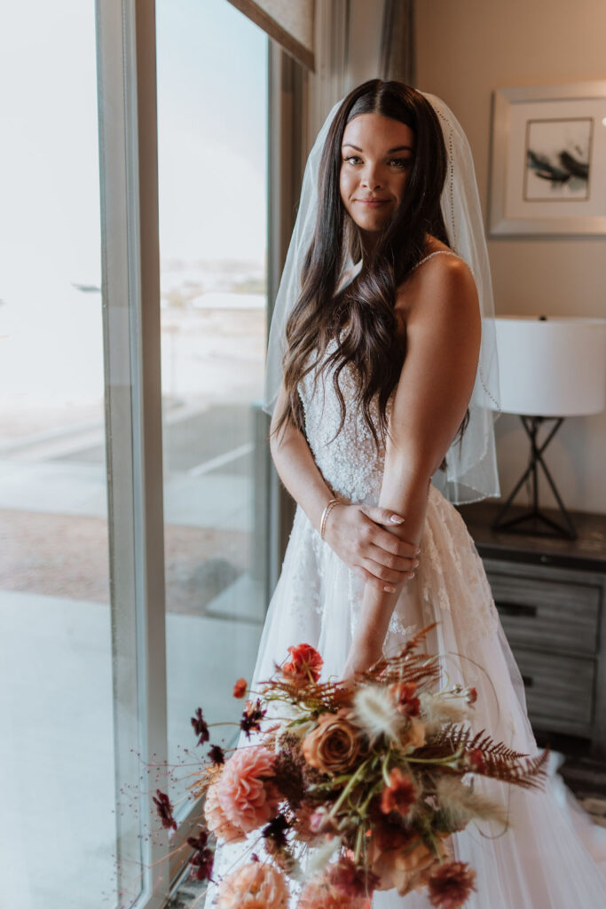 bride poses at window holding wedding bouquet 