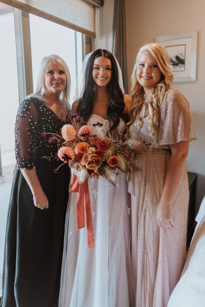 bride poses with bridesmaid and mom during wedding getting ready 