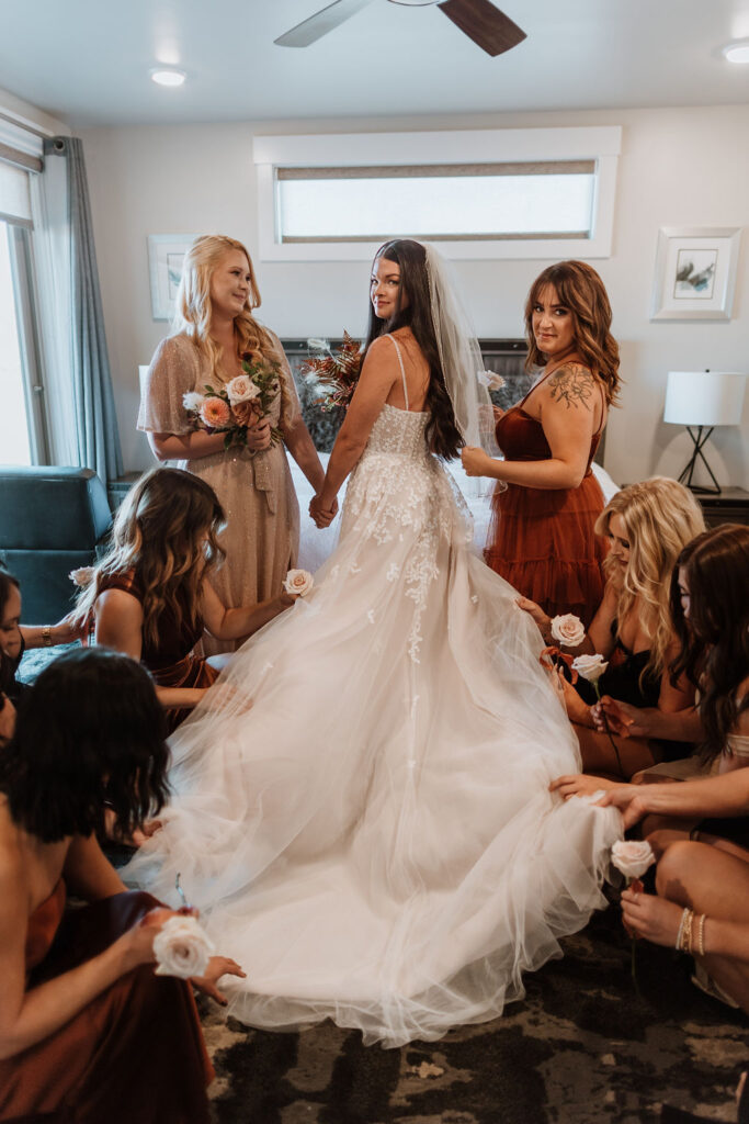 bride poses with bridesmaids holding wedding dress with roses