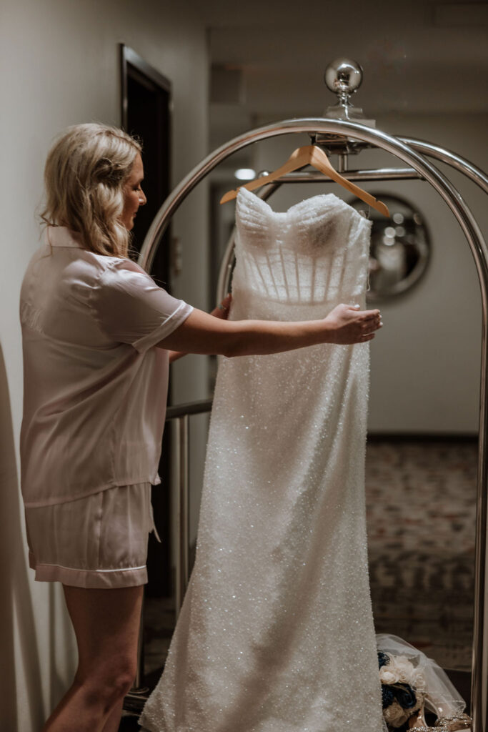 bride holds wedding dress hanging on cart 