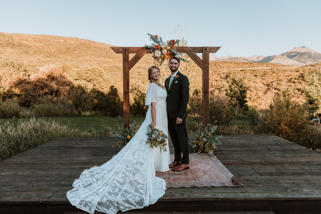 couple stands together under wedding floral arch