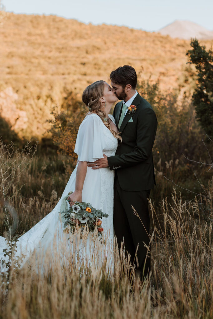 couple kisses in meadow at Whispering Oaks Ranch sunset wedding