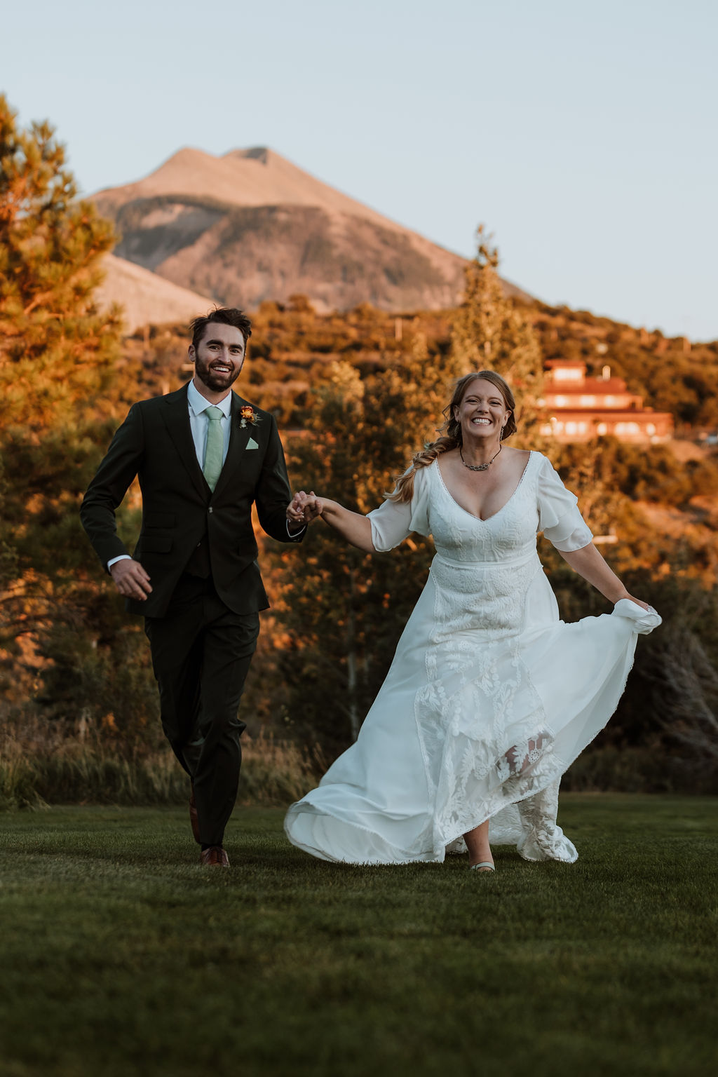 couple runs holding hands through sunset field under mountain