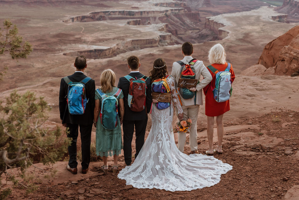 wedding guests wear backpacks with couple at adventure elopement